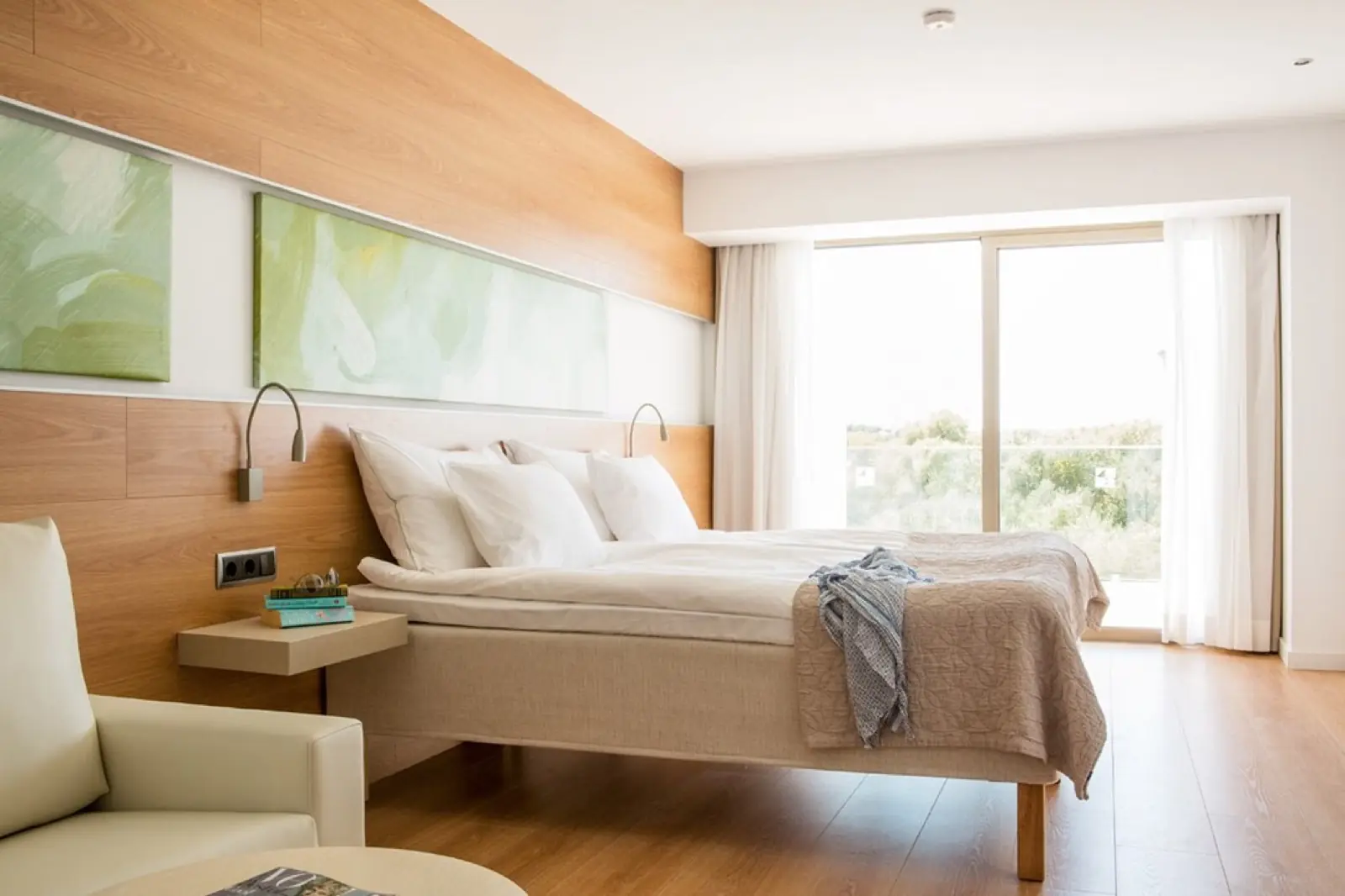 A Prime room with an oak feature wall, a private balcony framing trees, white linen and a folded grey throw at the foot of the bed