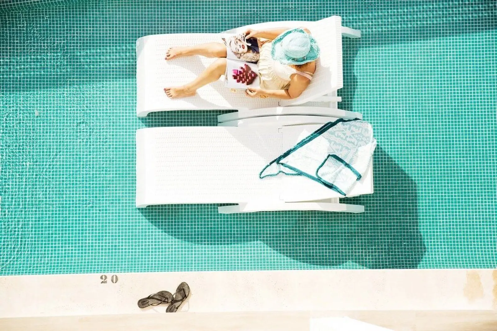 A ground-floor room terrace opening straight onto a turquoise swim-up pool, a towel over a chair and a glass of juice on a small table in the midday sun
