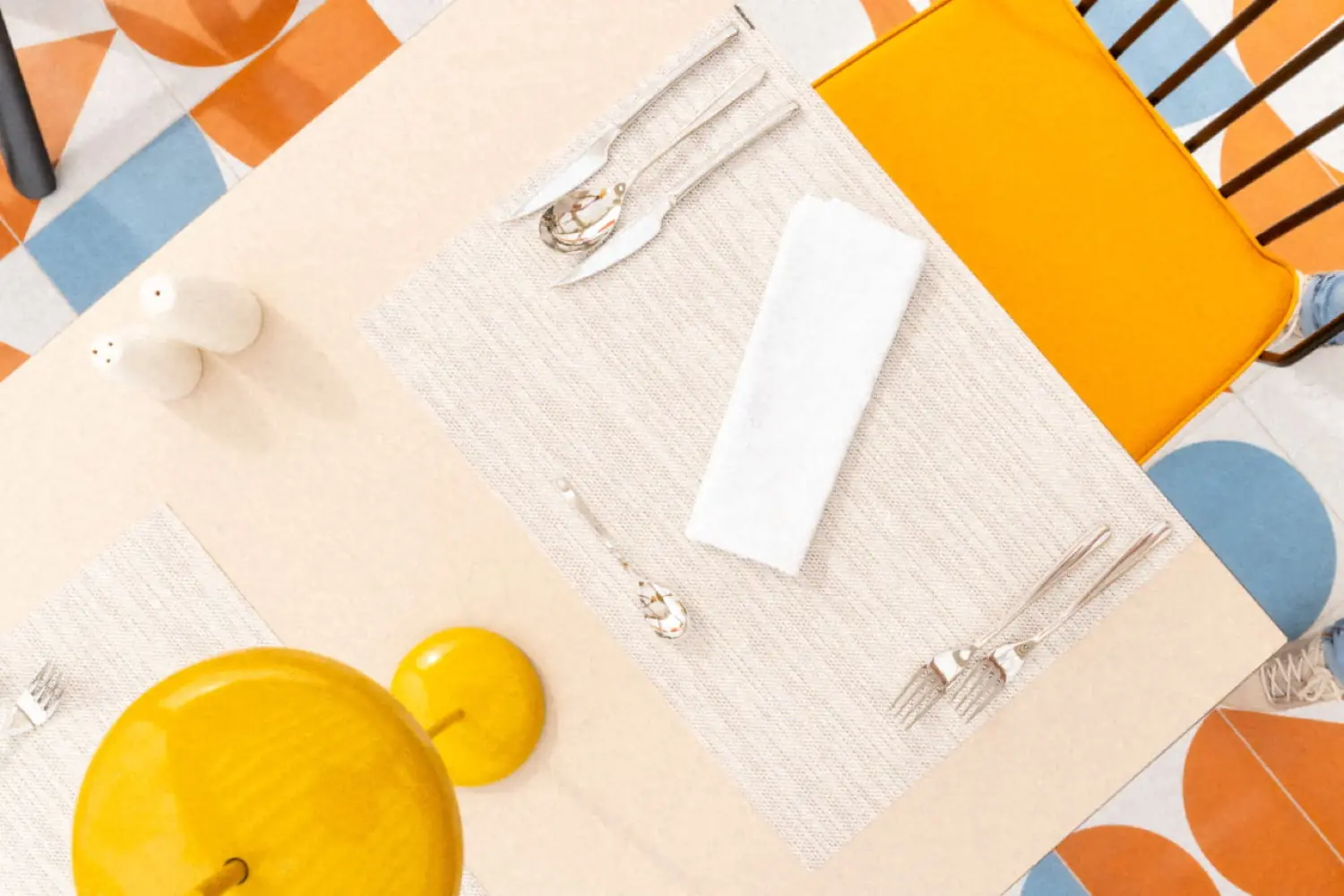 A Nua table laid from above, linen placemat and silver against a graphic floor of orange and blue tiles
