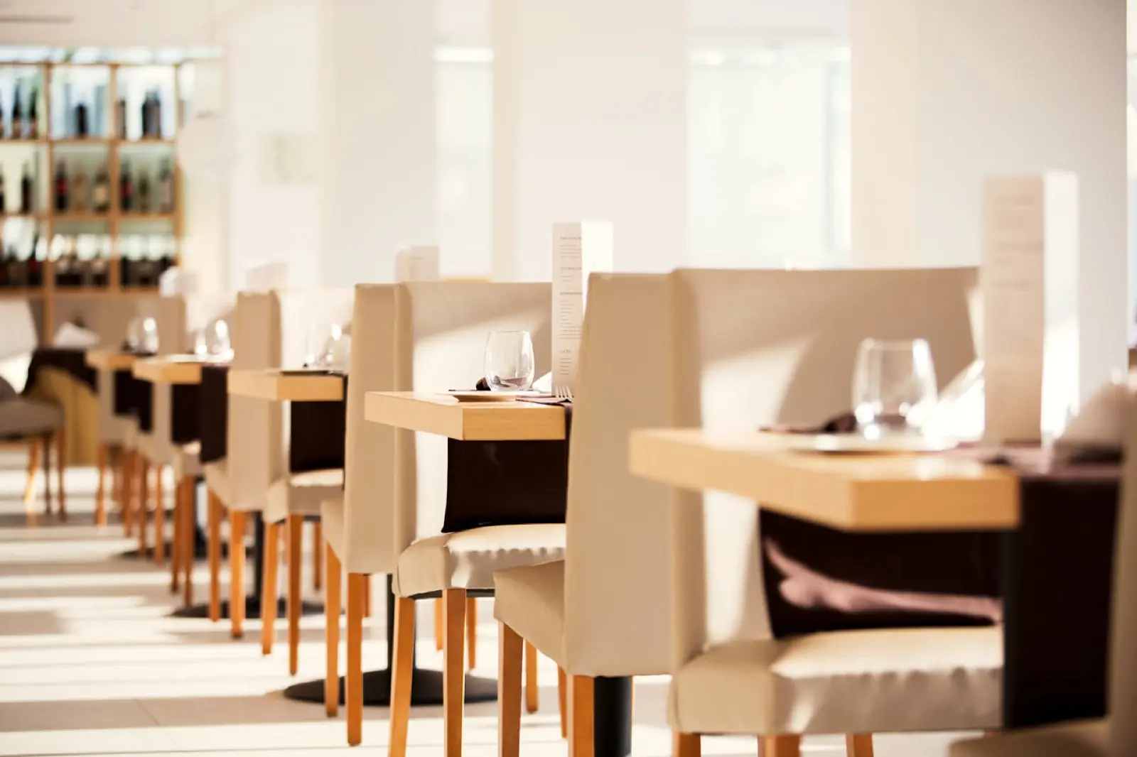 The main dining room with a long run of set tables, oak and cream chairs in soft daylight